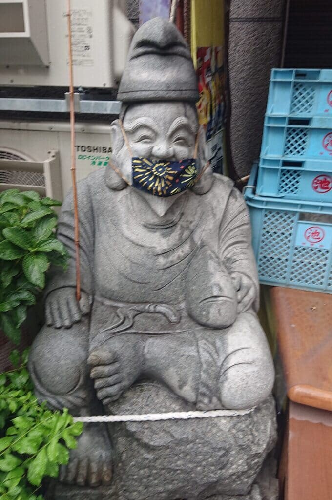 An Ebisu statue wearing a protective face mask.
